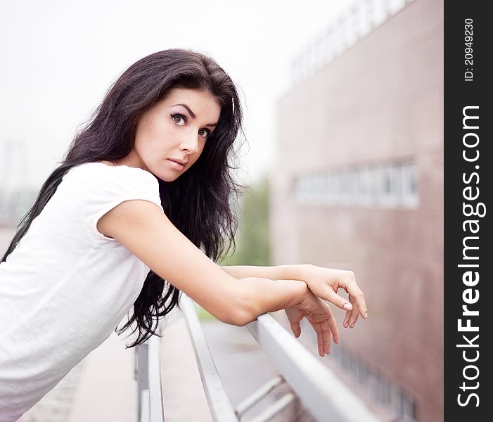 Very beautiful upset young brunette woman near the fence in the street. Very beautiful upset young brunette woman near the fence in the street