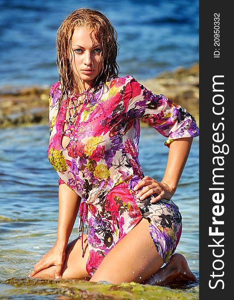 The beautiful young woman on a beach in a wet dres