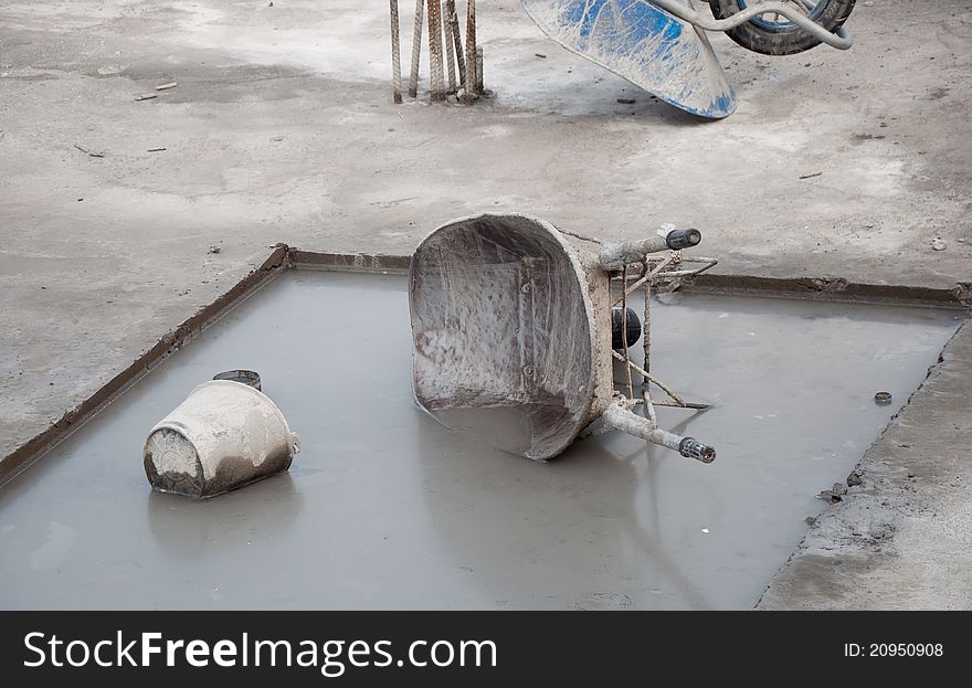 Untidy construction site with a wheelbarrow and bucket lying in dirty water.