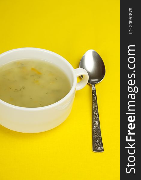 White bowl of soup on a yellow background next to a spoon is. White bowl of soup on a yellow background next to a spoon is
