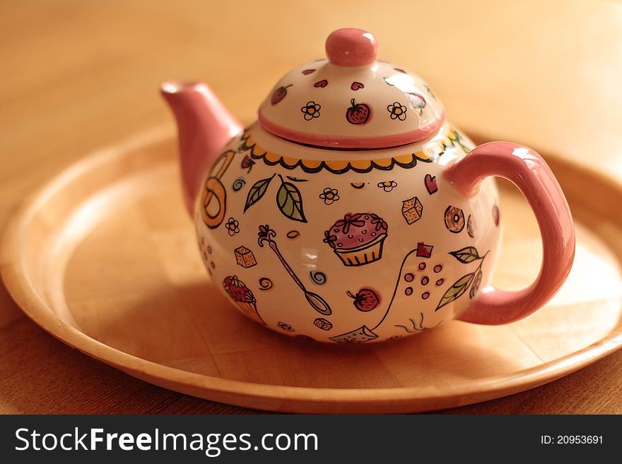 A cute pink teapot on the table with cartoony cupcake design. A cute pink teapot on the table with cartoony cupcake design.