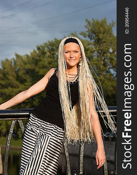 Young woman with braided locks standing on the bridge and smiling