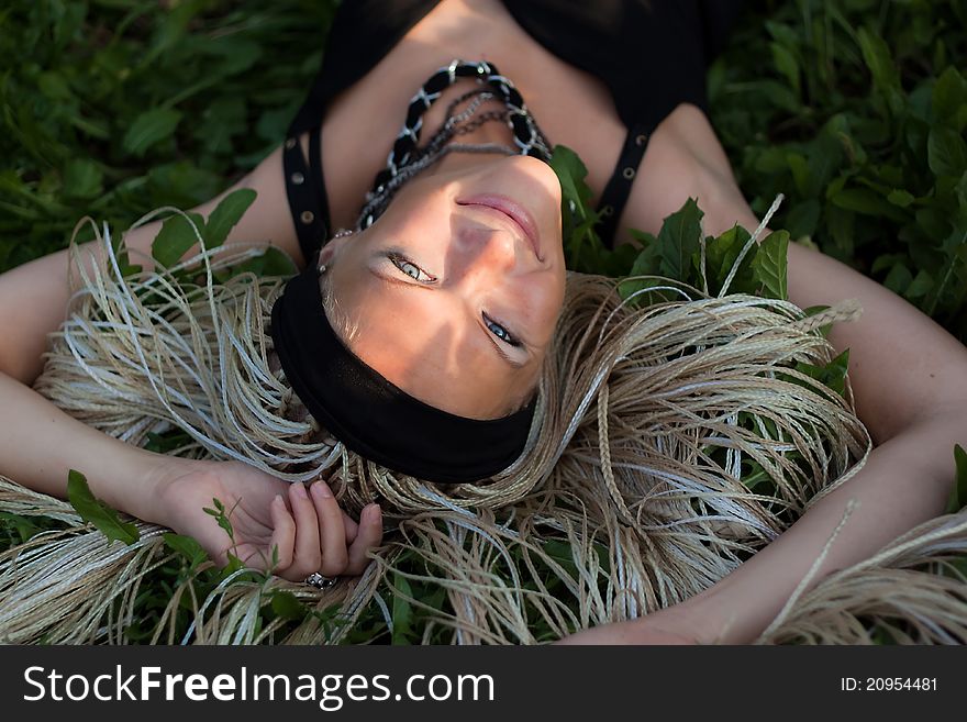 Young woman with braided lies on the grass. Sunlight on her face