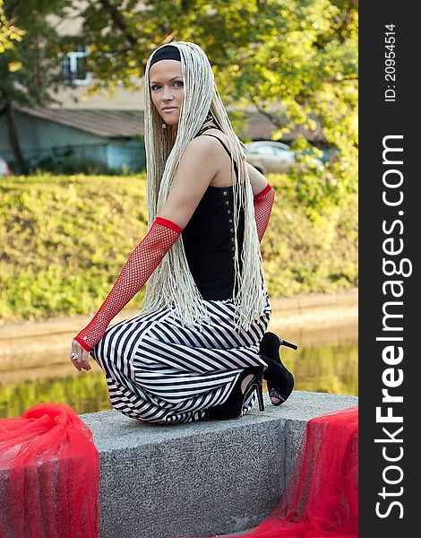 Young woman with braided seating near the river. On her hands are red gloves