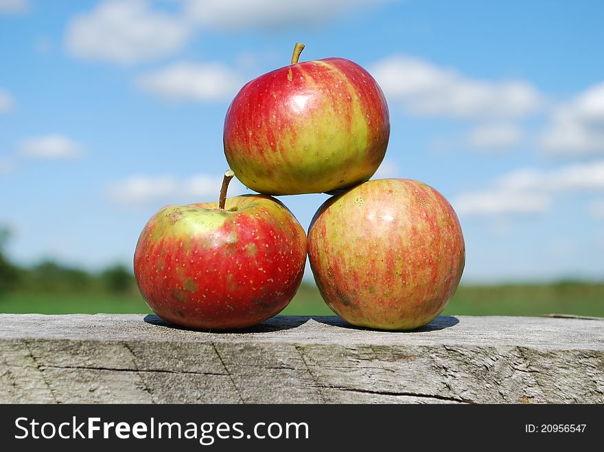 This is a stack of 3 apples sitting on a fence post. This is a stack of 3 apples sitting on a fence post.