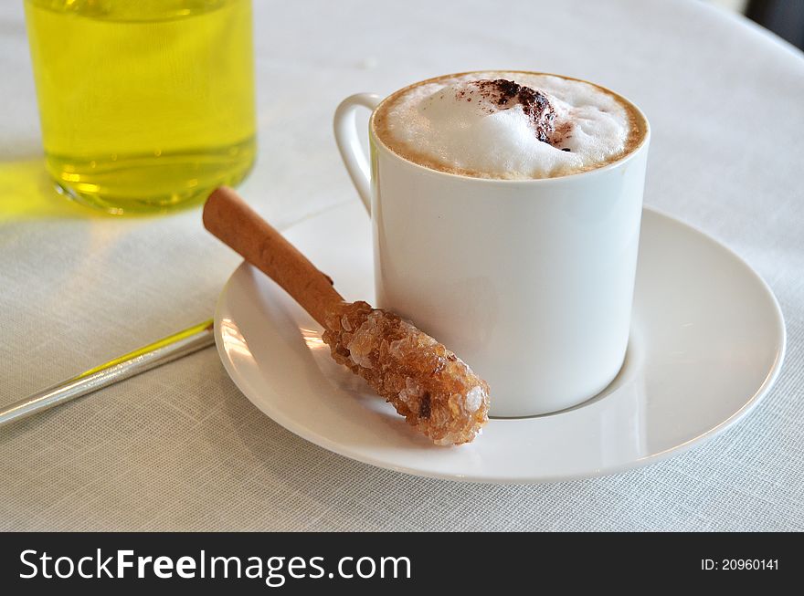 Cup of hot Cappuccino coffee on table with a bar of sugar and cinnamon