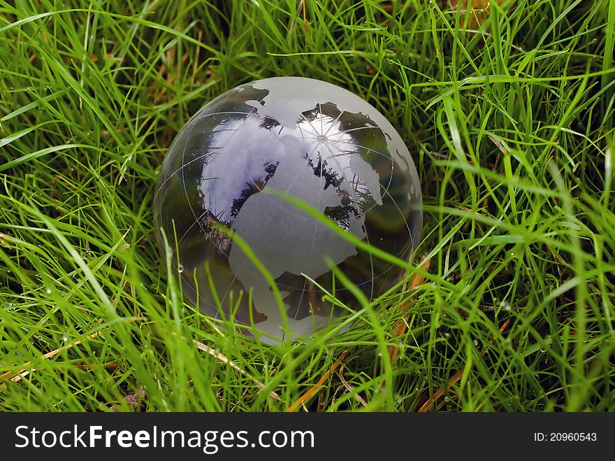 Crystal-clear globe in the green grass as protection and concern of environment