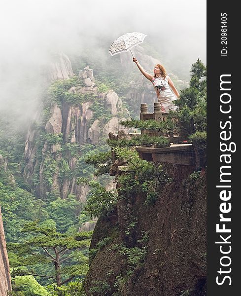 Portrait image of young woman with umbrella at cloudy weather on top of the Chinese mountain of Huangshan (yellow mountain). China, Asia. Portrait image of young woman with umbrella at cloudy weather on top of the Chinese mountain of Huangshan (yellow mountain). China, Asia.
