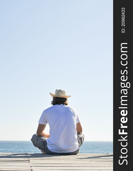 Young man sitting on the beach in straw hat. Young man sitting on the beach in straw hat