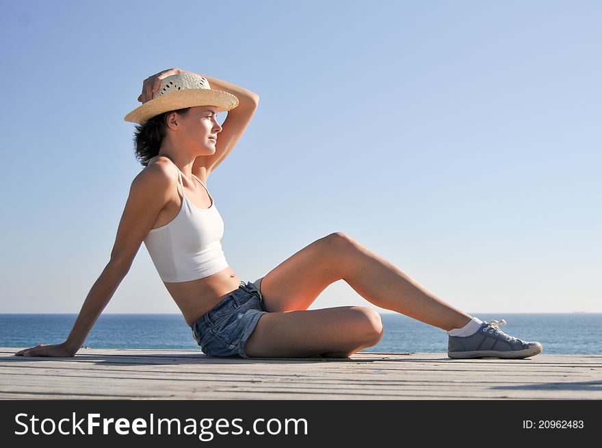Young woman sitting on the beach in straw hat. Young woman sitting on the beach in straw hat