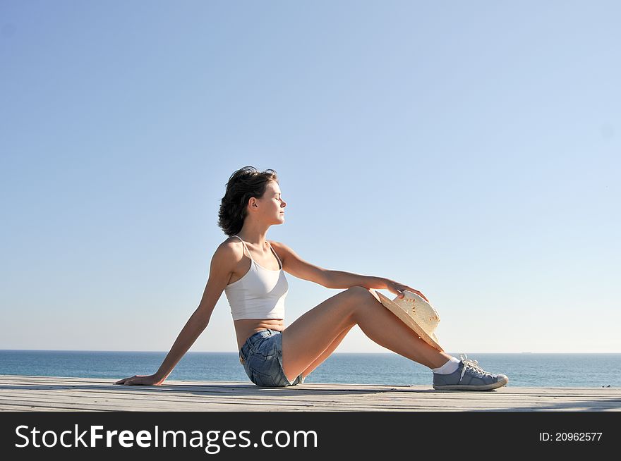 Young woman sitting on the beach in straw hat. Young woman sitting on the beach in straw hat