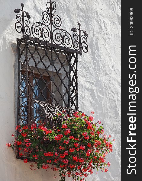 Old traditional Italian artistic window with iron portcullis and red geranium