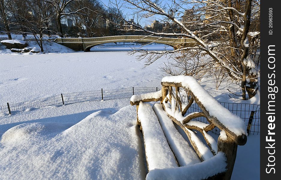 Central Park - New York City in front of the Bow brdige after snow storm with wooden bench. Central Park - New York City in front of the Bow brdige after snow storm with wooden bench