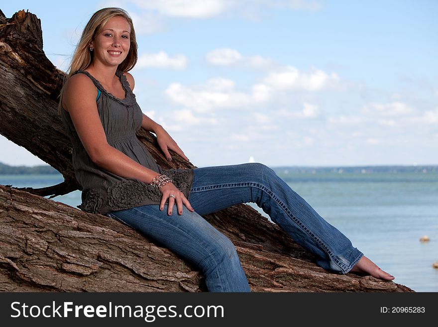 Beautiful young blond model posing on tree by lake. Beautiful young blond model posing on tree by lake