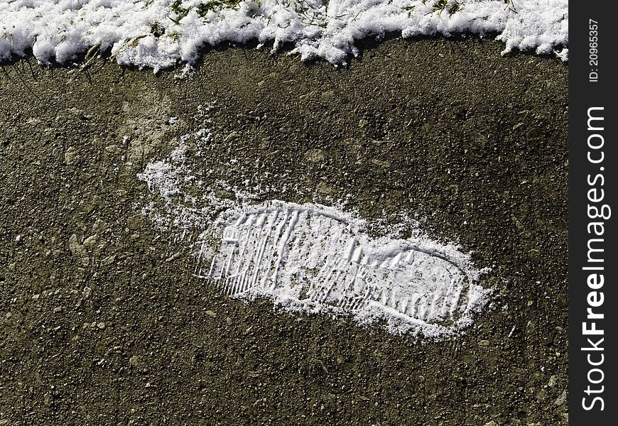 A boot print in the snow left on a bare are of soil. A boot print in the snow left on a bare are of soil.