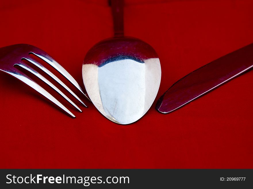 A cutlery set of a spoon, a fork, and a knife on red background. A cutlery set of a spoon, a fork, and a knife on red background