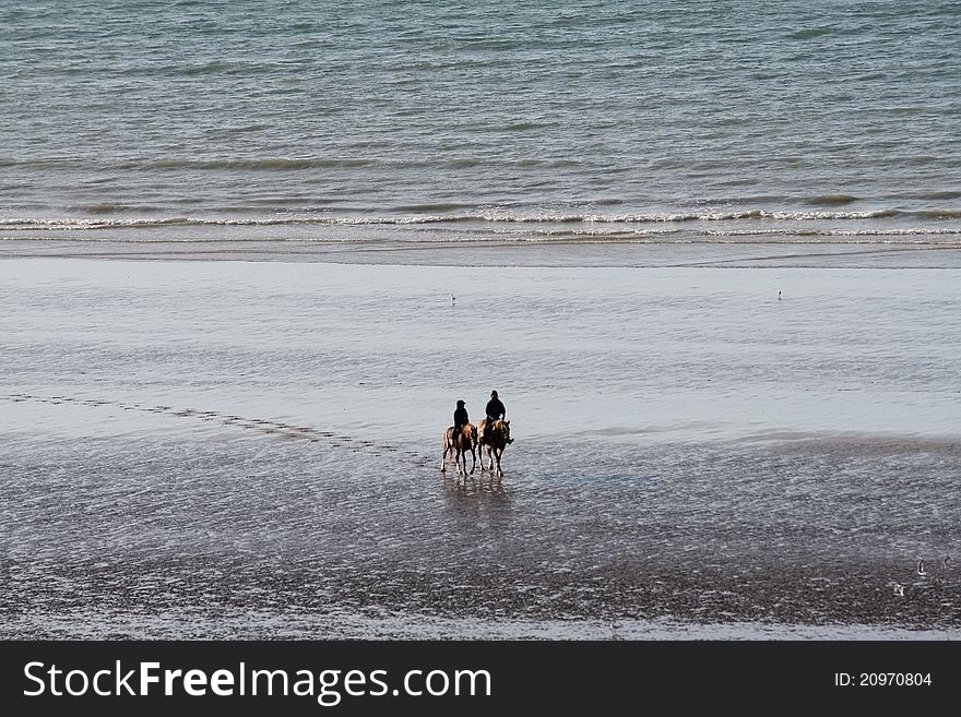 Two people horseback riding on the beach