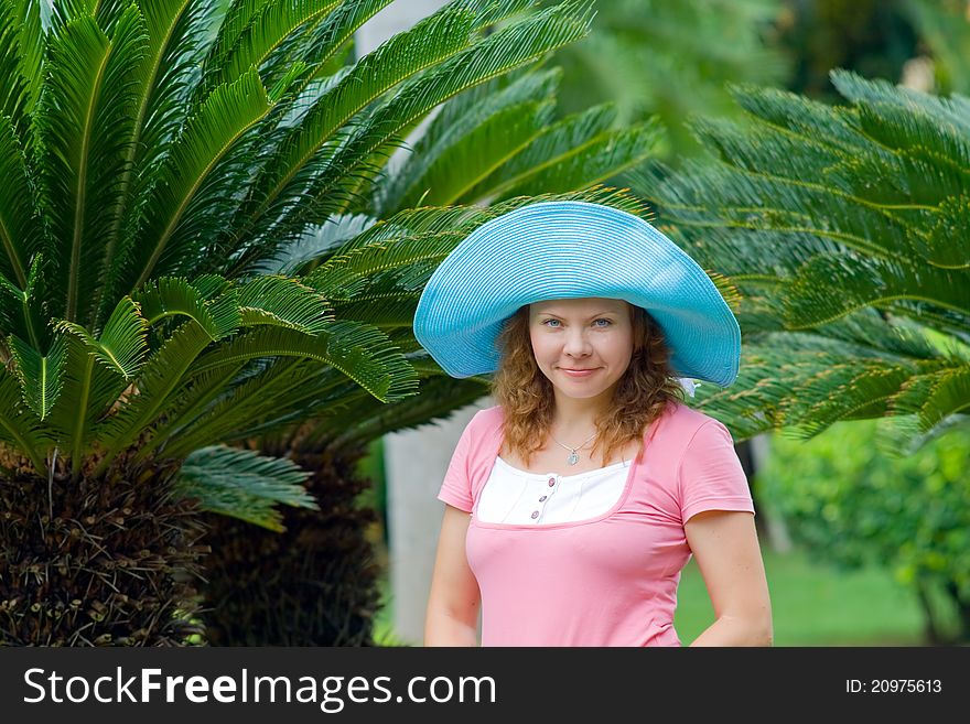 Portrait of beautiful young woman wearing bright blue hat in Palm's garden. Portrait of beautiful young woman wearing bright blue hat in Palm's garden.