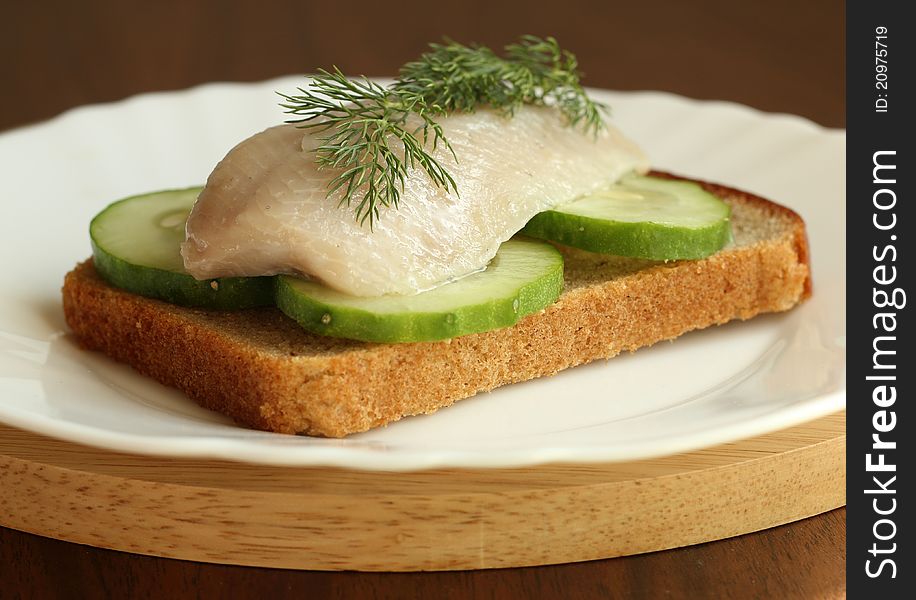 Herring on a piece of rye bread with cucumbers and dill