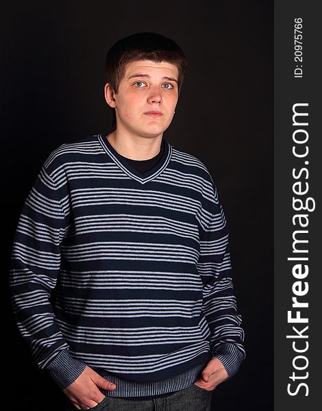 A young boy with his hands in pockets on the black background