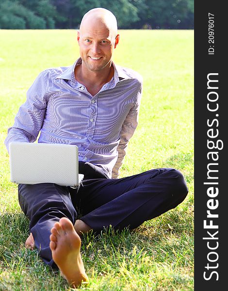 The young man sitting on a lawn works on the laptop. The young man sitting on a lawn works on the laptop