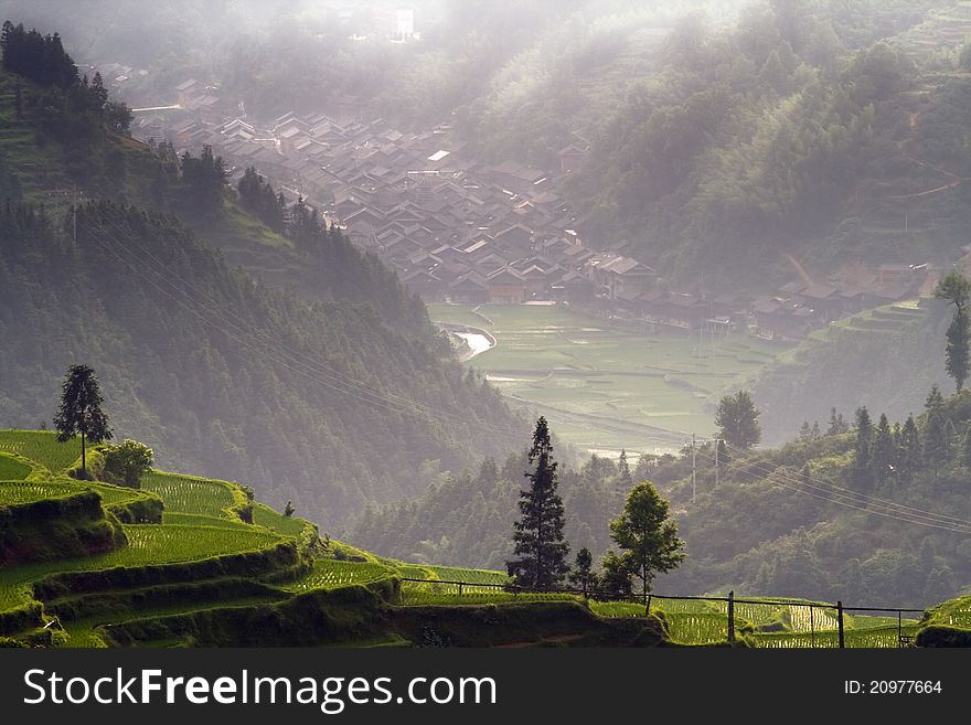 Zhaoxing Dong Chinese Village on the rice terrace at sunset. View at mountain and rice terrace near the river at foggy weather.