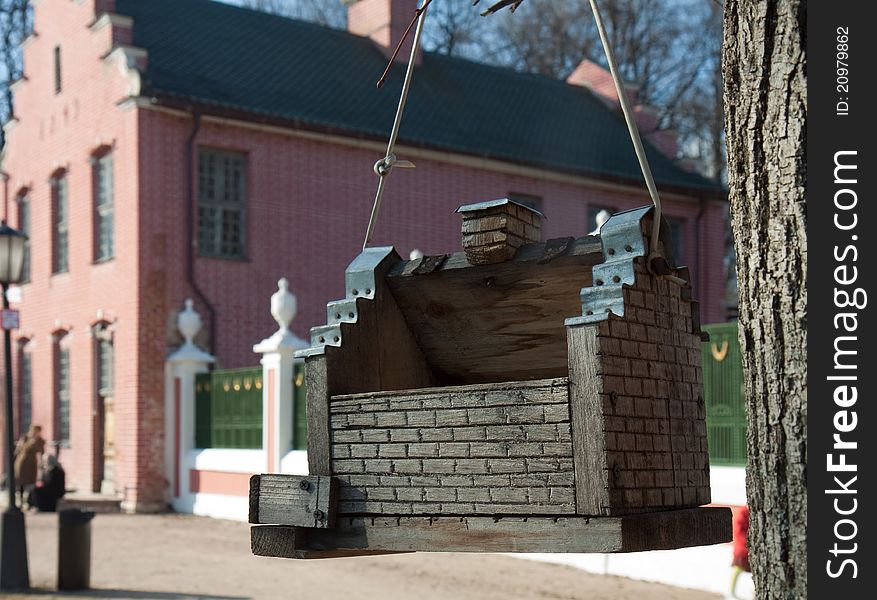 Wooden bird feeder hanging from a tree on a background of brick buildings of the eighteenth century in the park Kuskovo Moscow. Wooden bird feeder hanging from a tree on a background of brick buildings of the eighteenth century in the park Kuskovo Moscow