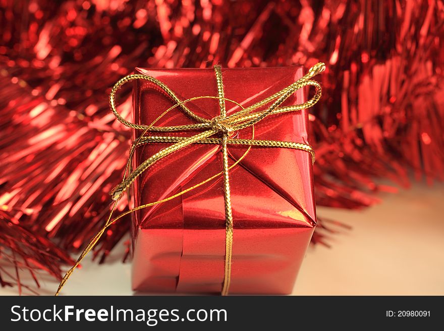 A single Christmas gift in red with gold string bows set against red tinsel.