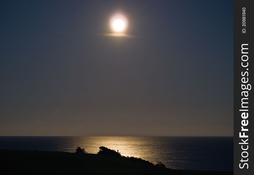 Full bright moon over the sea ocean with far away lights in the background. Full bright moon over the sea ocean with far away lights in the background