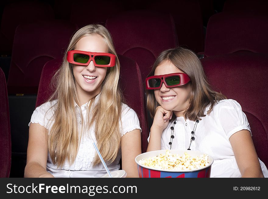 Two girls look three-dimensional cinema, sitting in the glasses, eat popcorn, drink drink. Two girls look three-dimensional cinema, sitting in the glasses, eat popcorn, drink drink