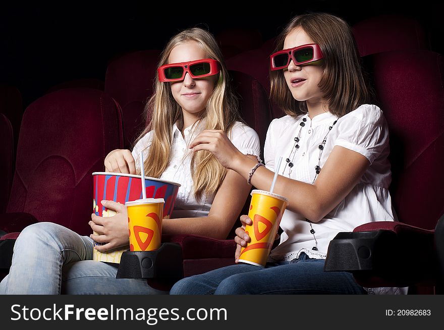 Two girls look three-dimensional cinema, sitting in the glasses, eat popcorn, drink drink. Two girls look three-dimensional cinema, sitting in the glasses, eat popcorn, drink drink