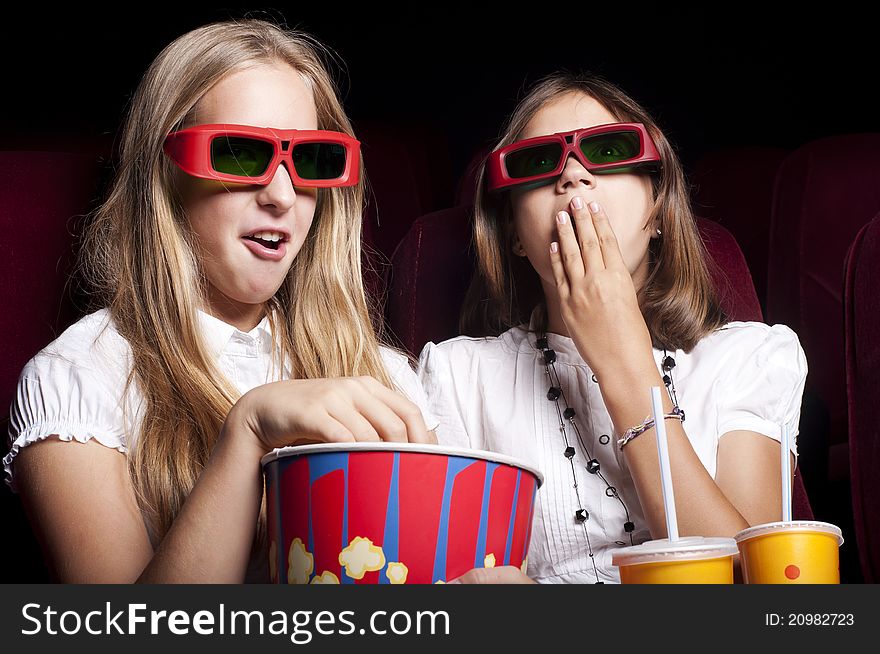 Two girls look three-dimensional cinema, sitting in the glasses, eat popcorn, drink drink. Two girls look three-dimensional cinema, sitting in the glasses, eat popcorn, drink drink