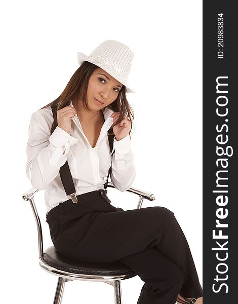 A woman in her hat and suspenders sitting on a stool with a serious expression on her face. A woman in her hat and suspenders sitting on a stool with a serious expression on her face.