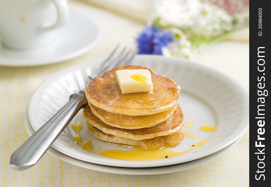 Pancakes with pat of melted butter on top and coffee in the background. Selective focus