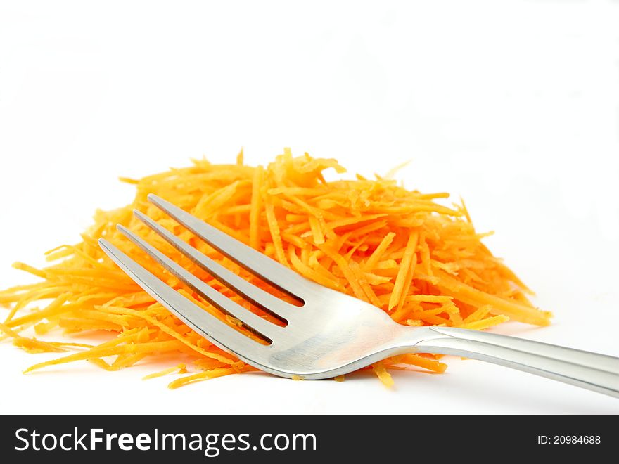 A lot of grated carrot and a fork on a white background. A lot of grated carrot and a fork on a white background