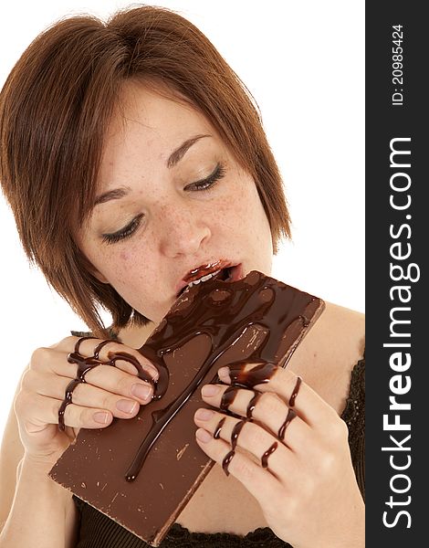 A woman taking a big bite of a chocolate candy bar with chocolate all over her hands. A woman taking a big bite of a chocolate candy bar with chocolate all over her hands.