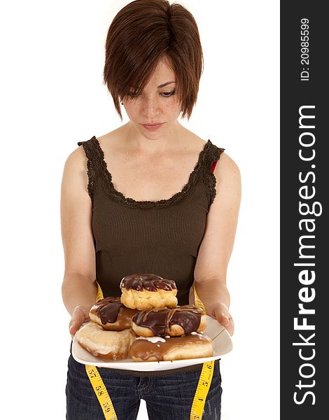 A woman knowing that the pile of doughnuts will add inches to her waist. A woman knowing that the pile of doughnuts will add inches to her waist.