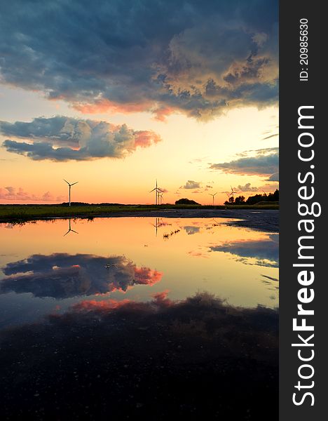An image of wind turbines reflection in the water at the sunset