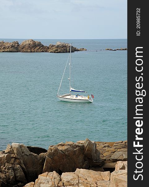 A yacht at anchor in a rocky bay. Blue sea and bold rocks. Guernsey, Channel Islands. A yacht at anchor in a rocky bay. Blue sea and bold rocks. Guernsey, Channel Islands.