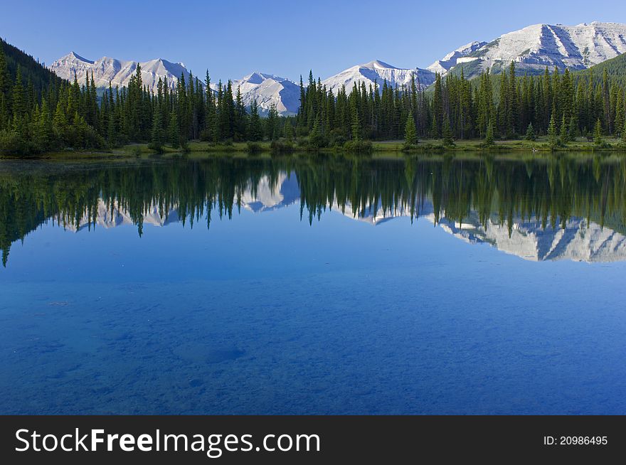 Forgetmenot Pond and reflections of mountains and evergreen trees in Kananaskis area of the Rocky Mountains Alberta