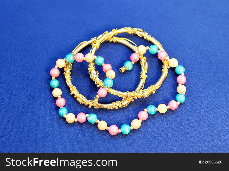 Colorful pearl chains with gold bangles on blue background