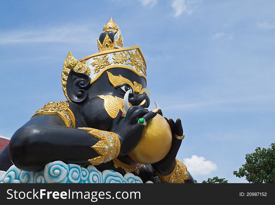 Statue of black deity called Rahu and blue sky background.