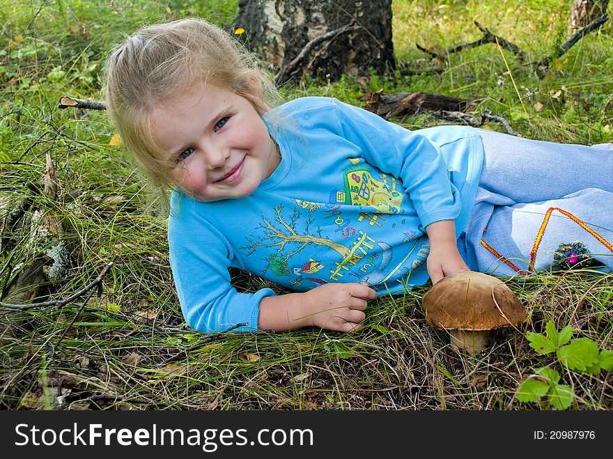 The child lays on a grass nearby the mushroom grows. The child lays on a grass nearby the mushroom grows