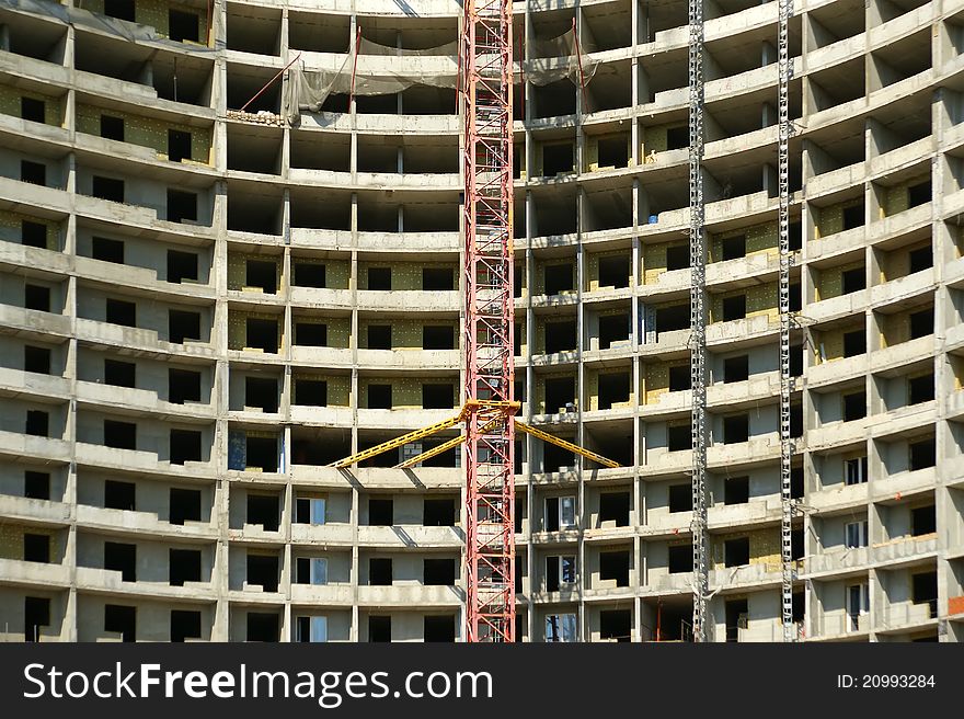 Building crane at the background of a multi-storey building under construction