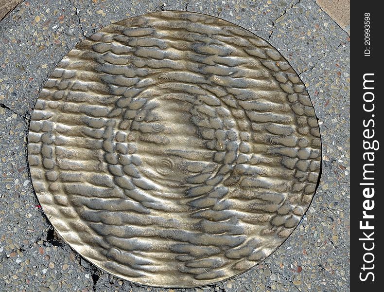 Grunge brass manhole cover on pavement