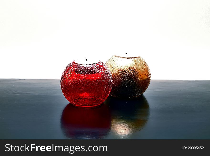 Two candles, shiny red and shiny gold, laying on black surface with white background with nice reflection on black.