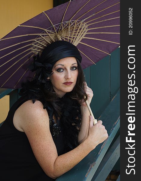 Close up of a Beautiful Woman dressed in 1930/40's Vintage clothing, hat and boa holding a purple paper umbrella at an old train depot. Close up of a Beautiful Woman dressed in 1930/40's Vintage clothing, hat and boa holding a purple paper umbrella at an old train depot.