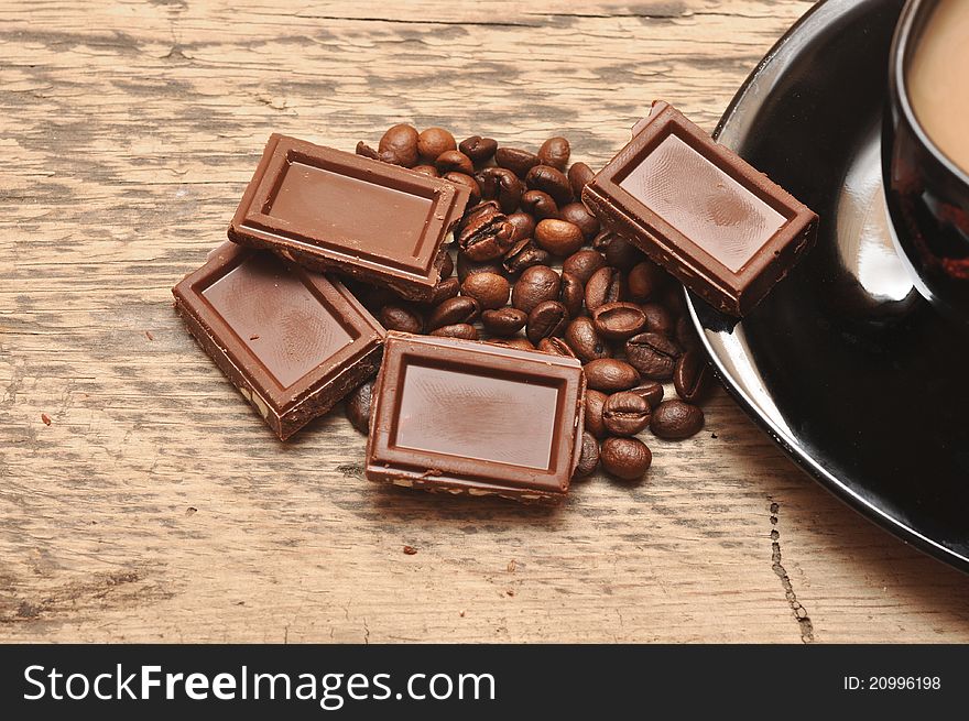 Closeup of freshly prepared cup coffee with beans and chocolate on wood background