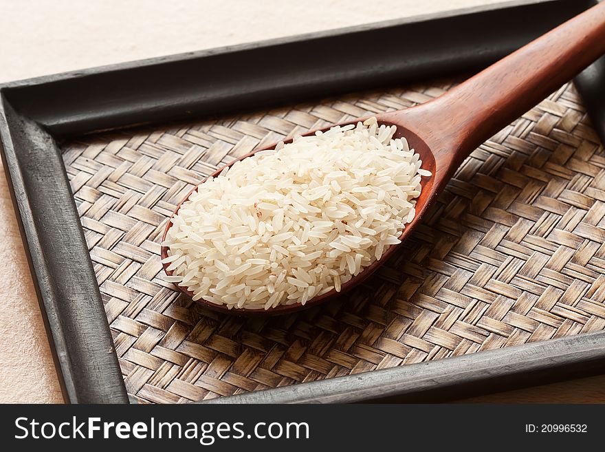 Raw rice in spoon on woven wood tray