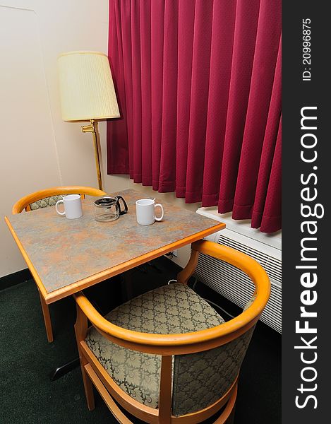 White drinking glasses on table with chairs and red curtain.